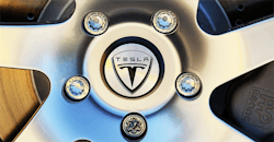 Telsa logo surrounded by lug nuts on wheel Telsa logo surrounded by lug nuts on wheel