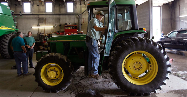Man standing on John Deere tractor in shop