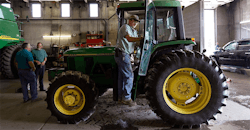 Man standing on John Deere tractor in shop Man standing on John Deere tractor in shop