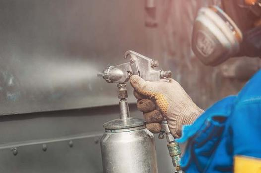 Worker spraying anti-corrosion coating on metal.