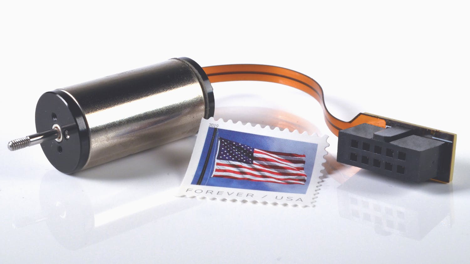 SDLM-016-032-01-01-M Direct Drive Linear Actuator against a white background with an American Forever stamp to show its made in America.