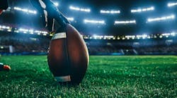 close-up shot of an American football being held by a football player on the stadium field at night with lights and crowd in the background. close-up shot of an American football being held by a football player on the stadium field at night with lights and crowd in the background.