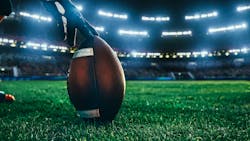 close-up shot of an American football being held by a football player on the stadium field at night with lights and crowd in the background. close-up shot of an American football being held by a football player on the stadium field at night with lights and crowd in the background.