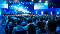Blurred presenter addressing a large audience at a corporate conference event. Blurred presenter addressing a large audience at a corporate conference event.
