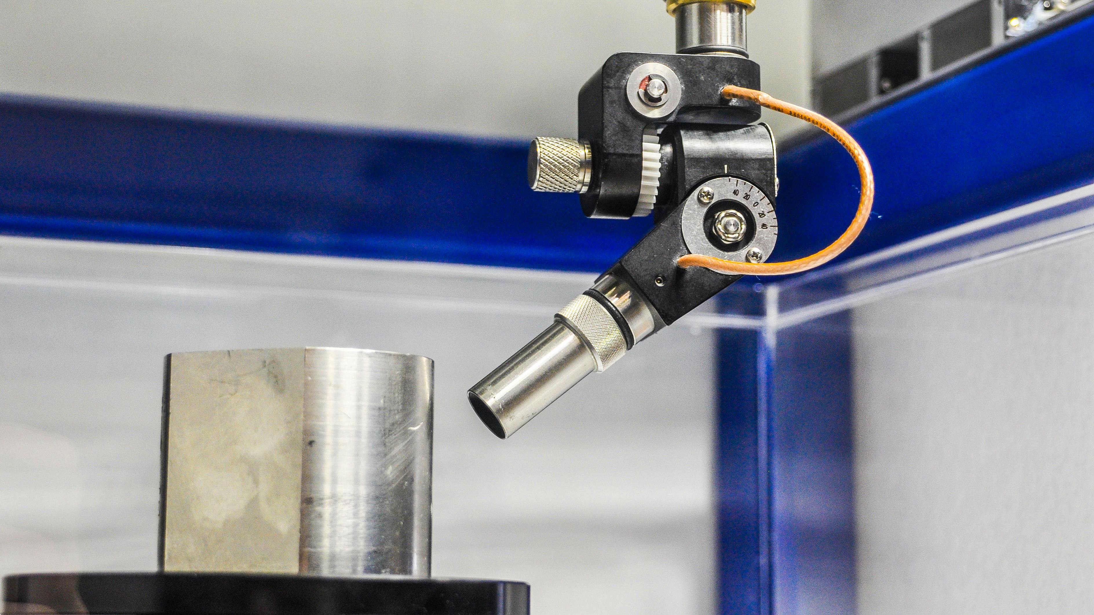 Close-up of the scanning acoustic microscopy process showing the transducer in use to inspect a metal part.