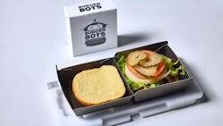 A BurgerBots burger box standing upright with another burger box open, showing an assembled burger inside, sitting on the QR code tray used in assembly on the shuttle conveyor. A BurgerBots burger box standing upright with another burger box open, showing an assembled burger inside, sitting on the QR code tray used in assembly on the shuttle conveyor.