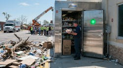 Worker accessing outdoor, large, stainless steel cold storage enclosure after natural disaster Worker accessing outdoor, large, stainless steel cold storage enclosure after natural disaster